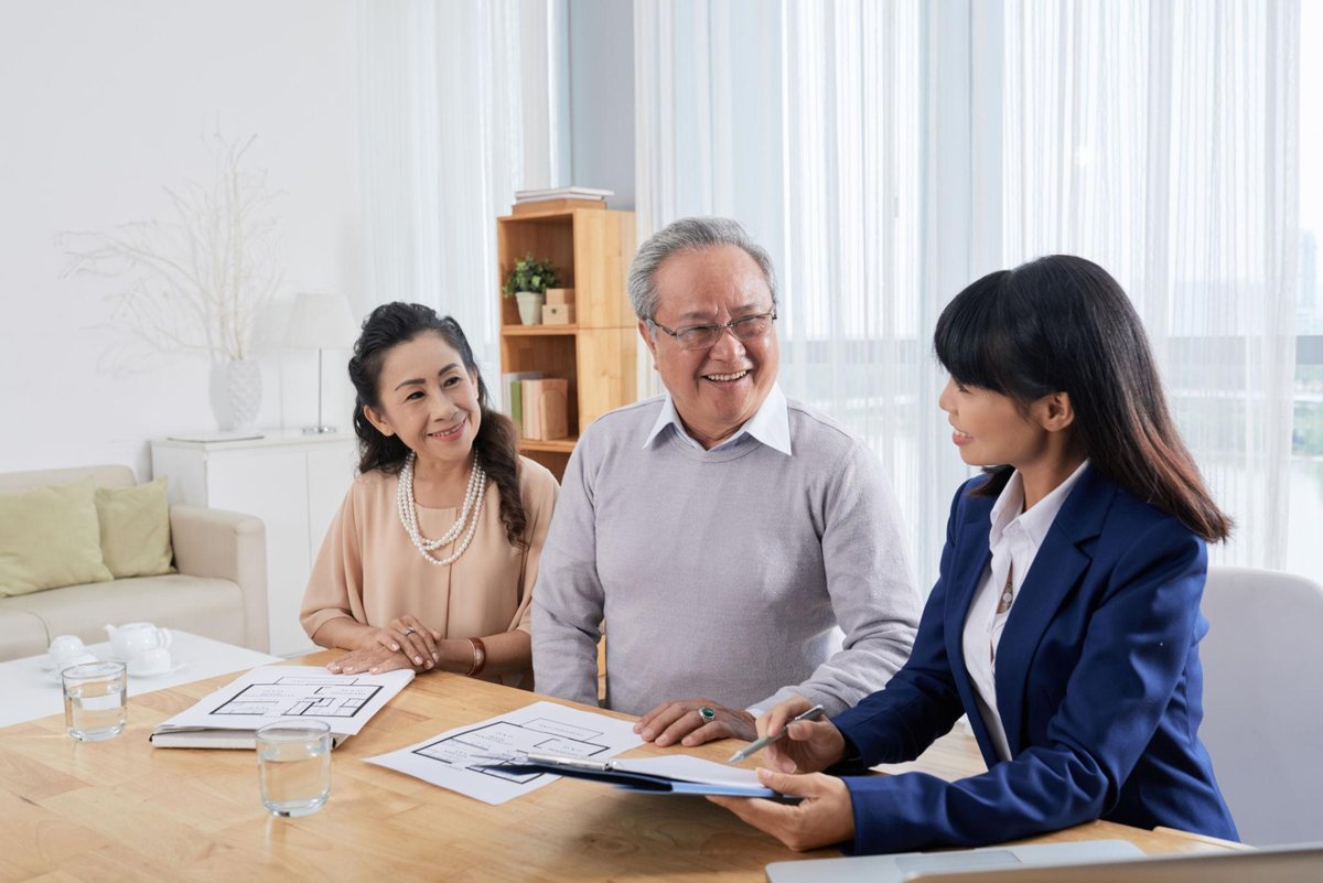 亞洲顧問向年長夫妻說明房屋委託合約與格局圖，三人面帶笑容